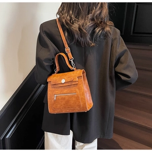 Detail of caramel vintage tote showing hand strap and front zipper pocket on wooden stairs