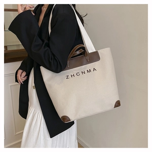 Detail of canvas tote bag with brown leather trim and ZHCNMA logo on female model