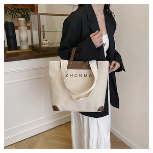 Close-up of a cream canvas tote bag with brown leather handles held by a model