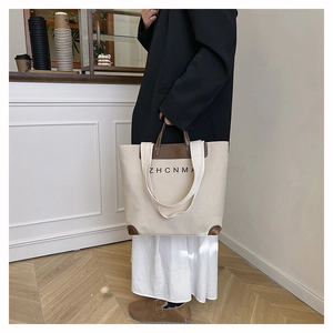 Detail of canvas tote bag with brown leather straps and ZHCNMA logo in a cafe setting