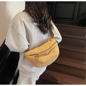 Detail of khaki crescent crossbody bag on a model walking on dark wooden stairs