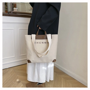 Detail of canvas tote bag featuring brown leather trim, ZHCNMA lettering and reinforced base
