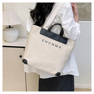 Detail view of cream canvas tote bag featuring black leather reinforced corners and trim