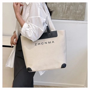 Detail of minimalist beige canvas tote bag with black leather reinforced corners and logo