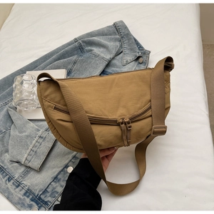 Flat lay of khaki crescent nylon crossbody bag on white linen with denim jacket detail