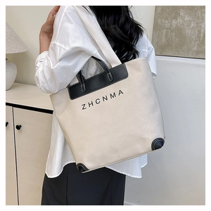 Detail of a large canvas tote bag with black leather trim and ZHCNMA logo print