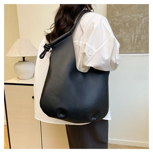 Detail of minimalist black tote bag with unique knot handle design on shoulder