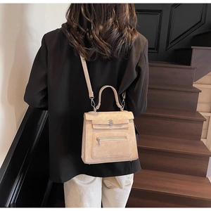 Detail of beige structured crossbody bag with textured finish shown on model on stairs