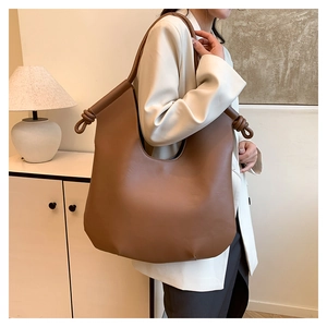 Close-up of knot design on large brown leather shoulder bag with white blazer style