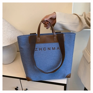 Close-up of blue denim tote bag with brown leather handles and ZHCNMA logo print
