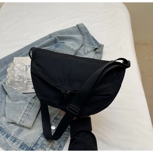 Detail of black nylon dumpling bag with adjustable strap on a denim jacket background