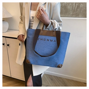 Detail of blue denim tote bag with brown leather trim and ZHCNMA logo on front