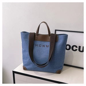 Detailed view of denim tote bag with brown leather handles and HCNM logo print