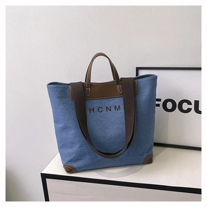 Detail view of denim tote bag with brown leather trim and HCNM logo on white counter
