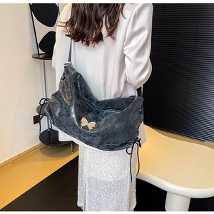 Dettaglio della borsa tote in pelle nera con logo a farfalla e coulisse decorative laterali