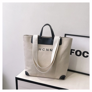 Detail of canvas tote bag with black leather patchwork handles and HCNM logo print