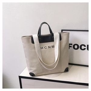 Detail shot of the HCNM canvas tote bag featuring black leather handles and trim