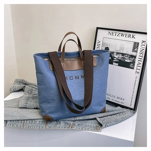 Detail of dark blue denim tote bag with brown leather handles and HCNM logo print