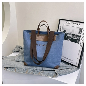 Detail of blue denim tote bag with leather corners and woven wide shoulder strap