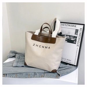 Detail of canvas tote bag with leather trim and ZHCNMA logo on a modern display stand