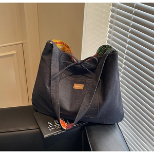 Detail of a navy denim tote bag featuring a leather logo patch and floral bow closure