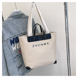 Detail of canvas tote bag with black leather handles and ZHCNMA logo hanging on a jacket