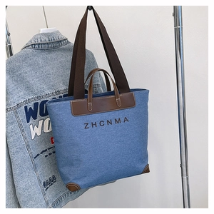 Detail of blue denim tote bag with leather handles and ZHCNMA logo on front