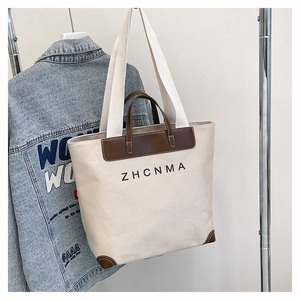 Detail of canvas tote bag with brown leather trim and ZHCNMA logo on metal hanger