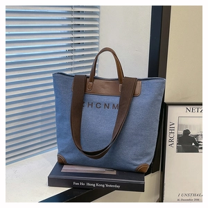 Detail of blue denim tote bag with brown leather handles and ZHCNM logo in home setting