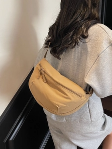 Minimalist khaki half-moon nylon crossbody bag with dual zippers worn by a model