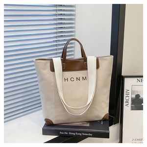Detail of canvas tote bag showing brown leather trim and HCNM embroidery on white canvas