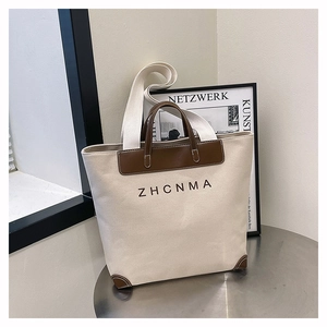 Close-up of beige canvas tote bag featuring brown leather trim and ZHCNMA logo detail