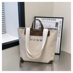 Detail of the large canvas tote bag with brown leather handles and HCNM logo print