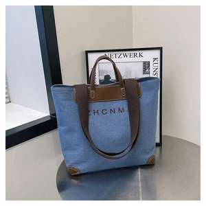 Detailed view of denim tote bag with leather straps and reinforced leather corners
