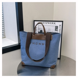 Close-up of a blue denim tote bag with brown leather handles and a woven shoulder strap