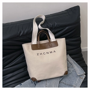 Detail of canvas tote bag with brown leather trim and ZHCNMA logo on a black sofa