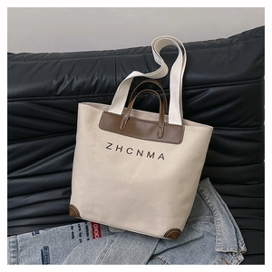 Detail of canvas tote bag with brown leather handles and ZHCNMA logo on a dark sofa