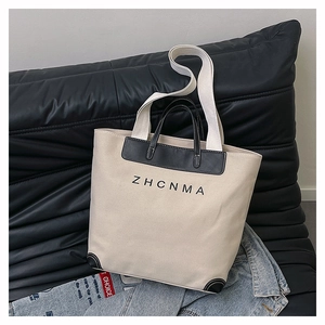 Close-up of beige canvas tote with black leather trim and ZHCNMA logo detail