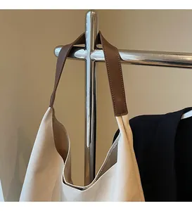 Détail de la bandoulière en cuir marron fixée à un sac cabas en toile beige