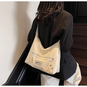 Close-up of cream tote bag with metallic studs and side zipper details on model