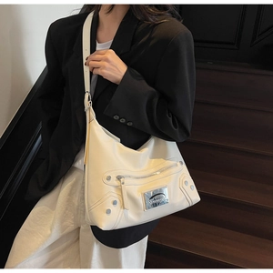 Detail of cream tote bag with metallic studs, zipper decor and adjustable shoulder strap