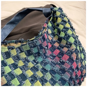Detailed view of multi-color checkerboard denim fabric with fringe trim on tote bag