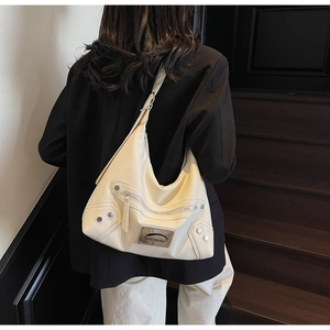 Close-up of beige moon-shaped tote bag with metallic logo plate and silver rivets details
