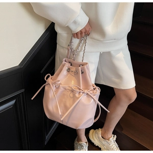 Pink glossy faux leather bucket bag featuring bow drawstring and silver chain strap