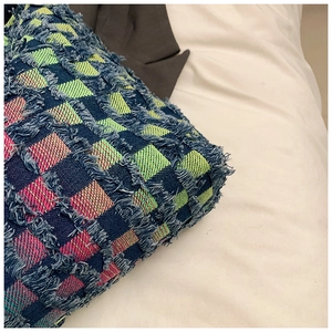 Macro shot of textured woven checkered fabric with blue, green, and pink fringe detail