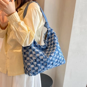 Detailed view of checkered denim tote bag with frayed edges worn by a model in a warm setting