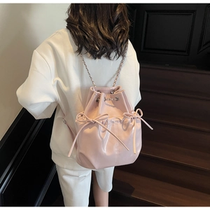 Pink faux leather bucket backpack with bow drawstrings and chain straps shown on a model