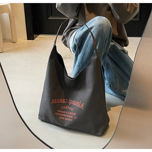 Détail d'un sac cabas en toile noire avec texte orange et fines lanières en cuir marron