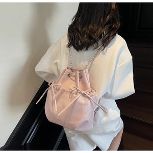 Detail of light pink bucket backpack featuring decorative bows and chain straps