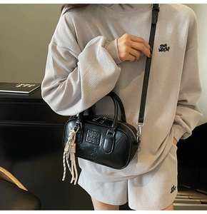 Détail d'un sac bowling noir en cuir texturé avec un pendentif en corde tressée